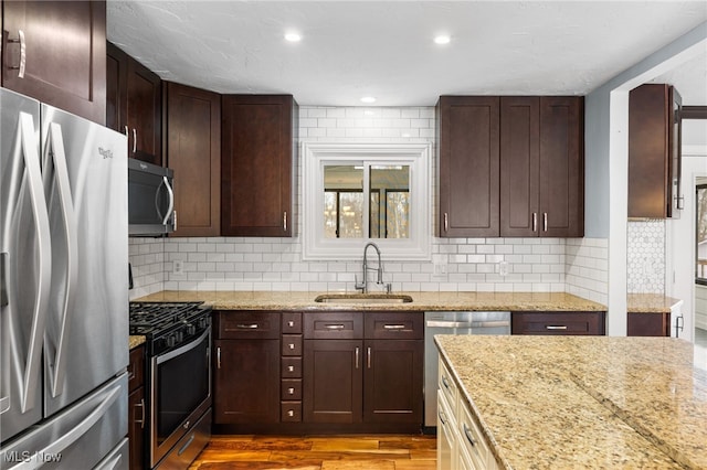 kitchen with light stone counters, wood finished floors, stainless steel appliances, and a sink