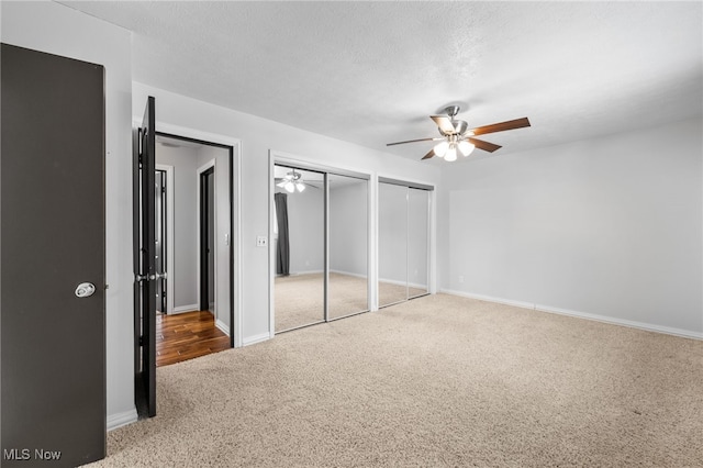 unfurnished bedroom featuring two closets, a ceiling fan, a textured ceiling, carpet floors, and baseboards