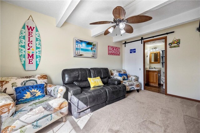 carpeted living area featuring beam ceiling, ceiling fan, baseboards, and a barn door