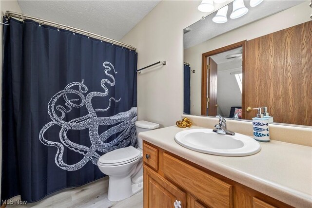 bathroom featuring toilet, vanity, a shower with curtain, wood finished floors, and a textured ceiling