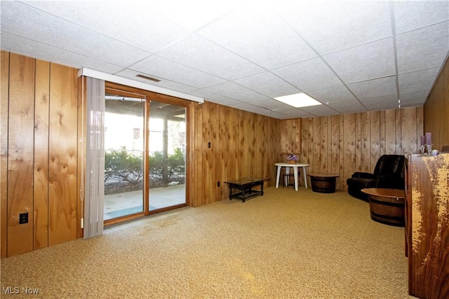 unfurnished room with a drop ceiling, visible vents, carpet, and wood walls