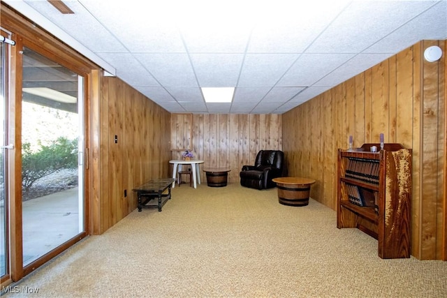 sitting room with wooden walls, carpet flooring, and a drop ceiling