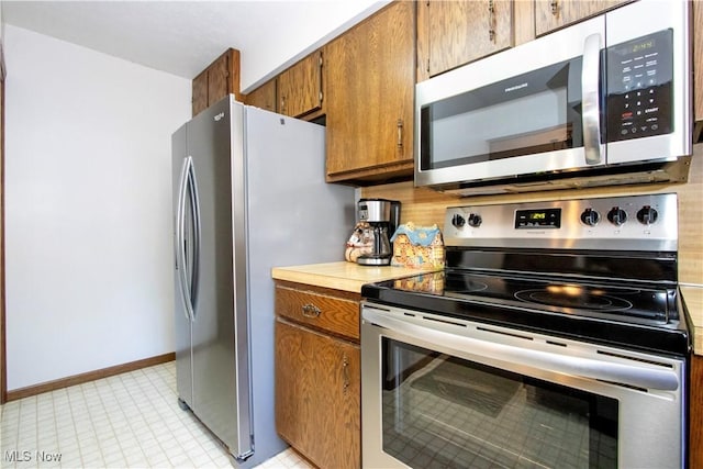 kitchen with brown cabinets, stainless steel appliances, light countertops, decorative backsplash, and baseboards