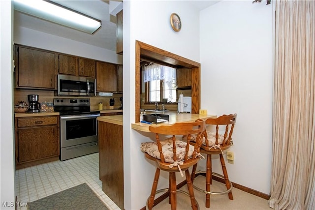 kitchen featuring baseboards, a breakfast bar, light countertops, stainless steel appliances, and a sink