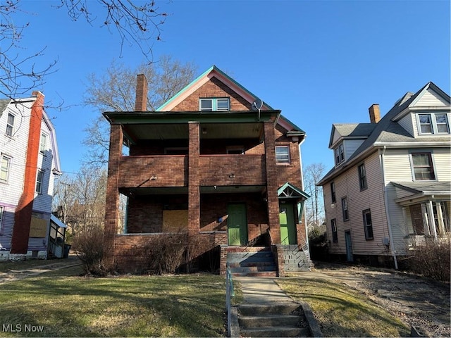 view of front of house with a front lawn, a balcony, brick siding, and a chimney