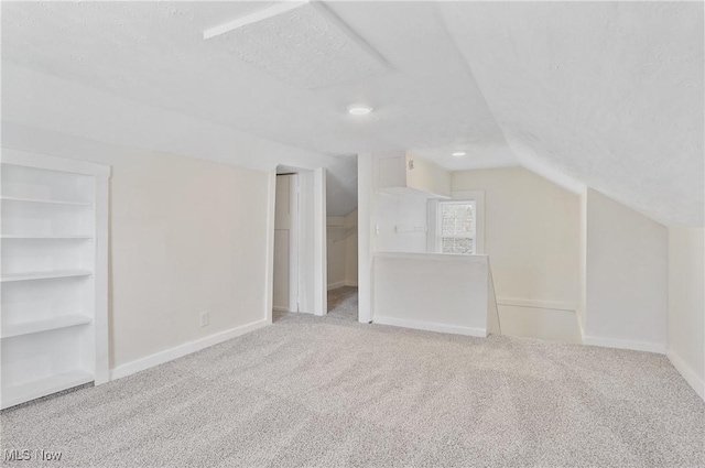 additional living space with built in shelves, baseboards, carpet, vaulted ceiling, and a textured ceiling