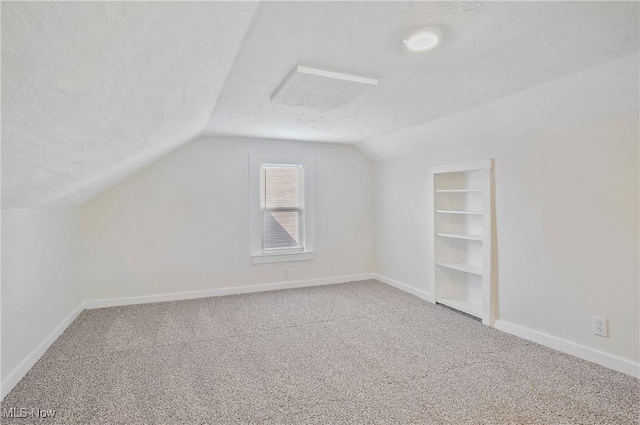 additional living space with built in shelves, baseboards, carpet floors, vaulted ceiling, and a textured ceiling