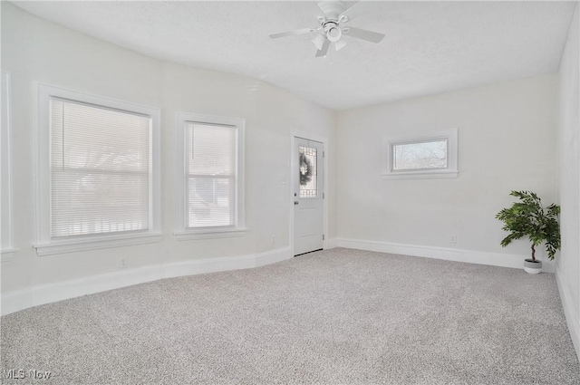 carpeted empty room with a healthy amount of sunlight, a ceiling fan, and baseboards