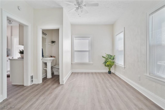 unfurnished bedroom featuring visible vents, baseboards, light wood-style floors, ensuite bath, and a textured ceiling