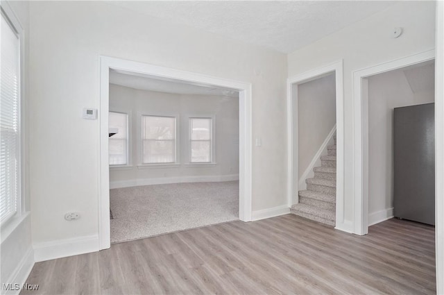 empty room featuring stairway, light wood-style flooring, a textured ceiling, and baseboards