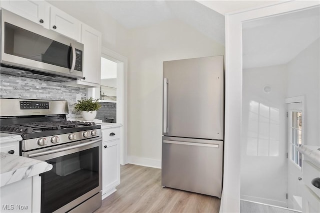 kitchen featuring light wood-type flooring, light stone counters, backsplash, appliances with stainless steel finishes, and white cabinets