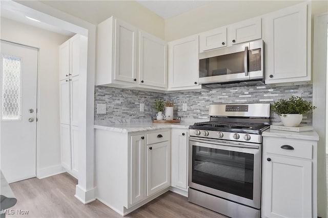 kitchen featuring light stone countertops, decorative backsplash, light wood-style floors, appliances with stainless steel finishes, and white cabinetry