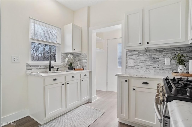 kitchen featuring a sink, light wood-style floors, stainless steel range with gas stovetop, and white cabinets