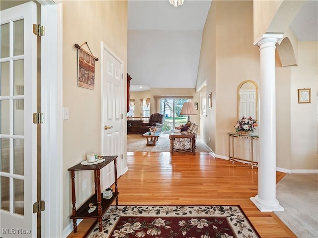 foyer featuring light wood finished floors, baseboards, ornate columns, and a towering ceiling