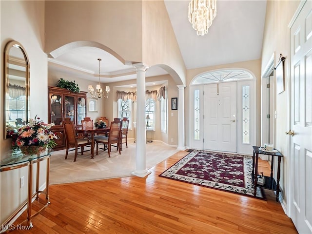 entrance foyer with ornate columns, an inviting chandelier, light wood-style flooring, arched walkways, and a towering ceiling