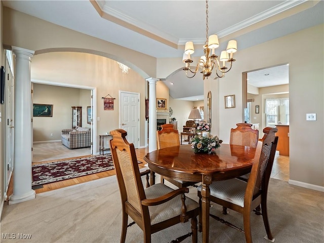 dining space featuring arched walkways, a fireplace, decorative columns, a raised ceiling, and light colored carpet