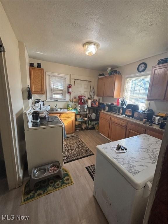 kitchen with a sink, stainless steel microwave, a textured ceiling, light wood finished floors, and range