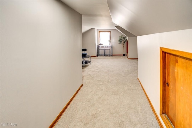 hallway with light colored carpet, baseboards, and vaulted ceiling