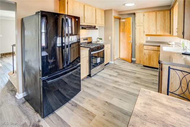 kitchen with stainless steel gas range oven, light wood-style flooring, light brown cabinetry, a sink, and freestanding refrigerator