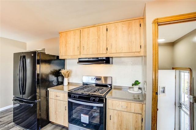 kitchen featuring ventilation hood, stainless steel gas stove, freestanding refrigerator, and light brown cabinetry