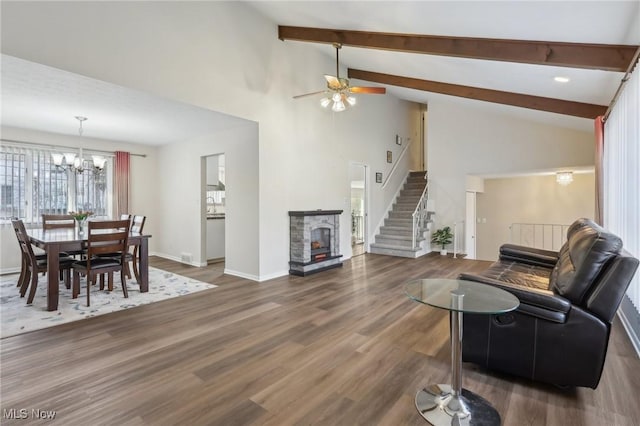 living room featuring wood finished floors, baseboards, lofted ceiling with beams, a stone fireplace, and stairs