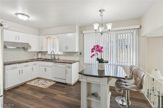 kitchen with dark countertops, dark wood-type flooring, under cabinet range hood, white dishwasher, and a sink