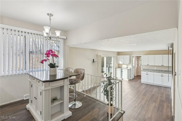 kitchen with visible vents, a kitchen island, dark wood finished floors, white cabinets, and a chandelier