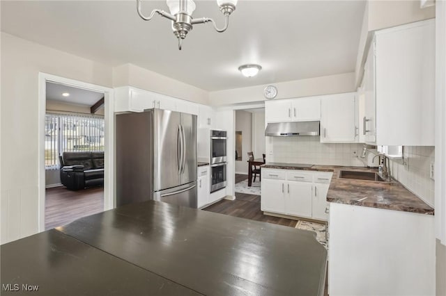 kitchen with dark countertops, under cabinet range hood, decorative backsplash, appliances with stainless steel finishes, and a sink