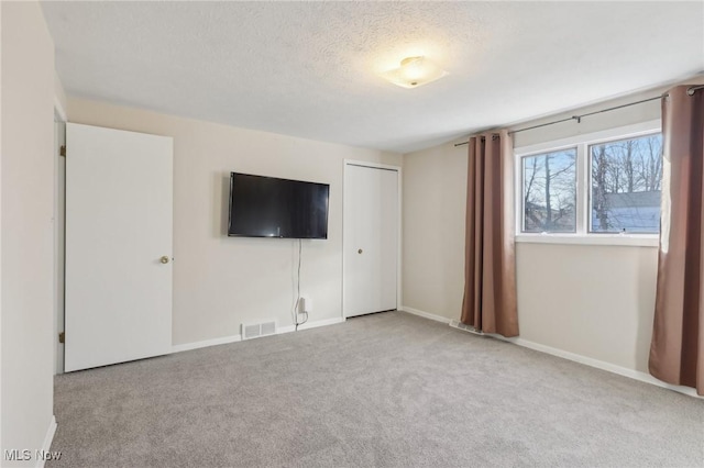 unfurnished living room featuring visible vents, baseboards, a textured ceiling, and carpet flooring