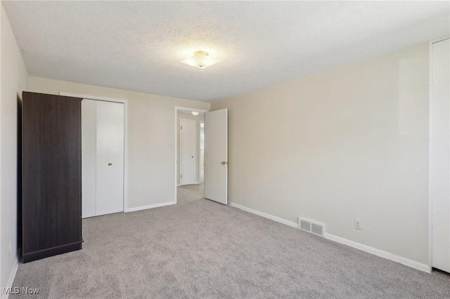 unfurnished bedroom featuring visible vents, baseboards, carpet floors, a closet, and a textured ceiling