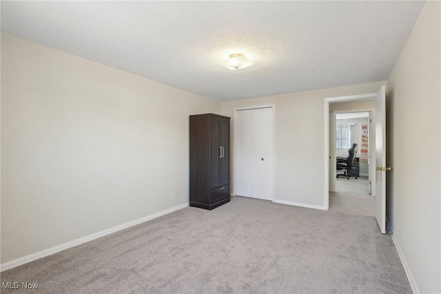 unfurnished bedroom with light colored carpet, baseboards, and a textured ceiling