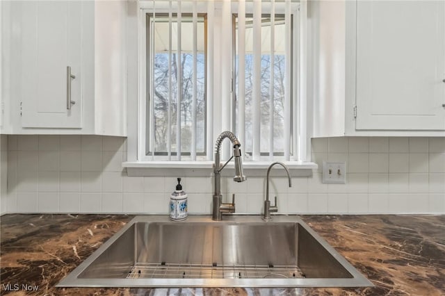 interior details featuring a sink, tasteful backsplash, and white cabinets