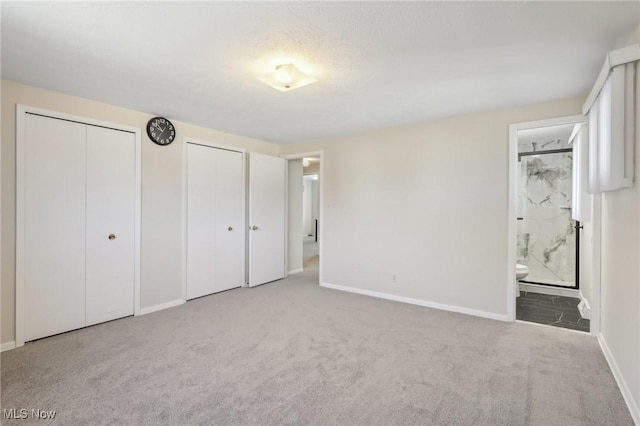 unfurnished bedroom with carpet flooring, connected bathroom, two closets, and baseboards