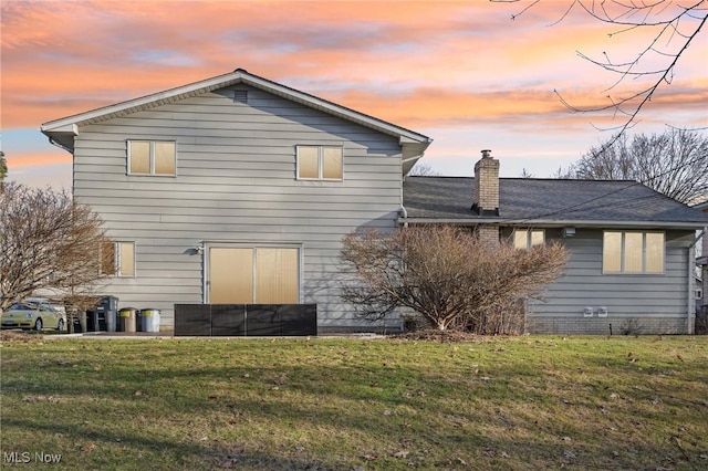 back of property at dusk featuring a chimney and a yard