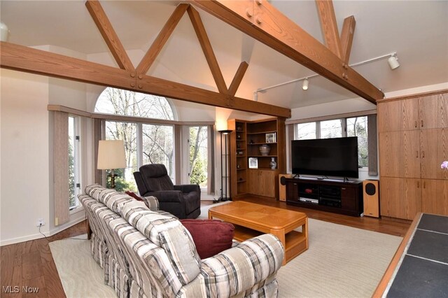 living area featuring beamed ceiling, wood finished floors, baseboards, and high vaulted ceiling