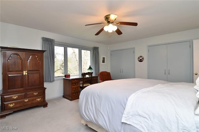 bedroom featuring light colored carpet, a ceiling fan, and multiple closets