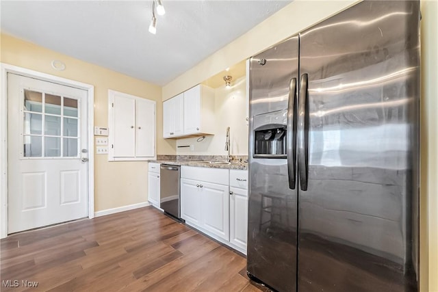 kitchen with dark wood-type flooring, a sink, appliances with stainless steel finishes, white cabinets, and light stone countertops