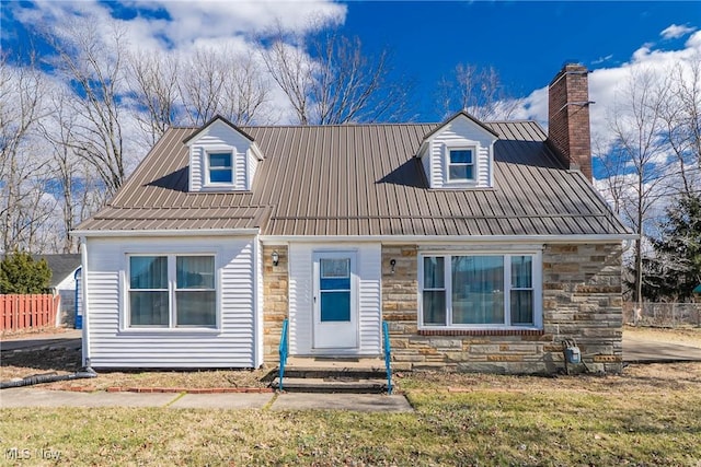 cape cod home with metal roof, stone siding, a chimney, and fence