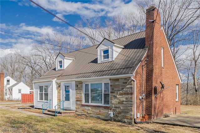 cape cod house featuring stone siding, a chimney, a front yard, and metal roof