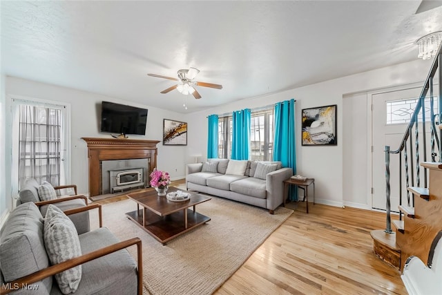 living area featuring stairs, light wood-style floors, baseboards, and a ceiling fan