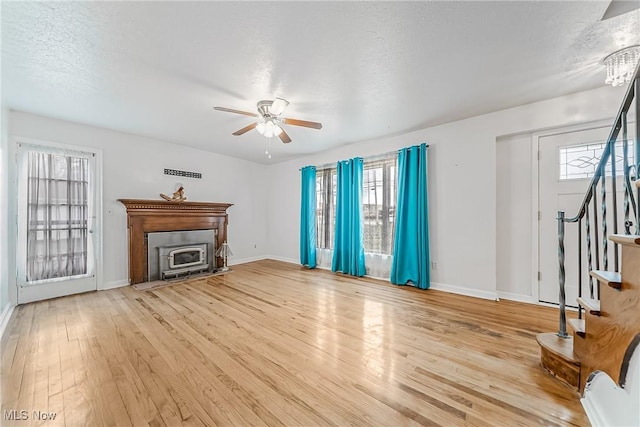 unfurnished living room with light wood-type flooring, a ceiling fan, a fireplace, baseboards, and stairs