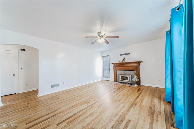 unfurnished living room featuring baseboards, visible vents, arched walkways, ceiling fan, and light wood-style floors