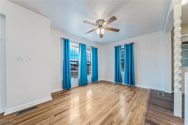 unfurnished room featuring a ceiling fan, wood finished floors, visible vents, and baseboards