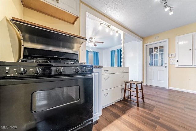 kitchen with black gas range oven, track lighting, dark wood-style flooring, and white cabinetry