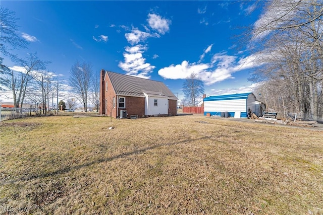 exterior space with a yard, a chimney, an outdoor structure, brick siding, and metal roof