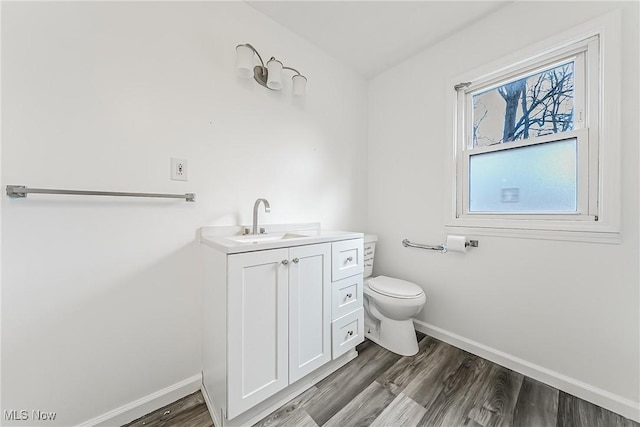 half bath with toilet, wood finished floors, and baseboards