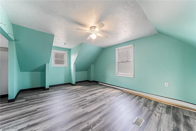 additional living space with visible vents, lofted ceiling, a textured ceiling, and wood finished floors