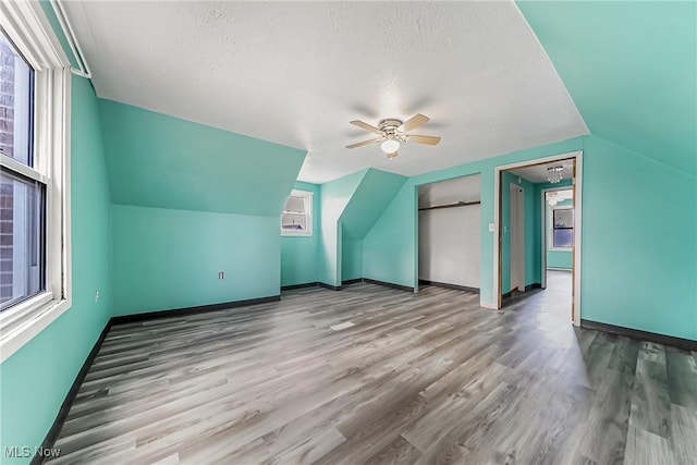 bonus room featuring a textured ceiling, wood finished floors, baseboards, and a healthy amount of sunlight