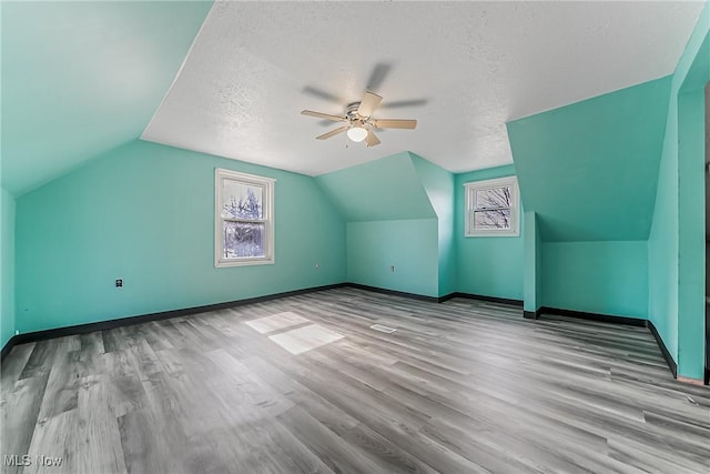 additional living space with baseboards, lofted ceiling, wood finished floors, a textured ceiling, and a ceiling fan