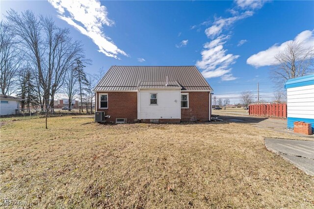 rear view of property featuring metal roof, brick siding, a lawn, and fence